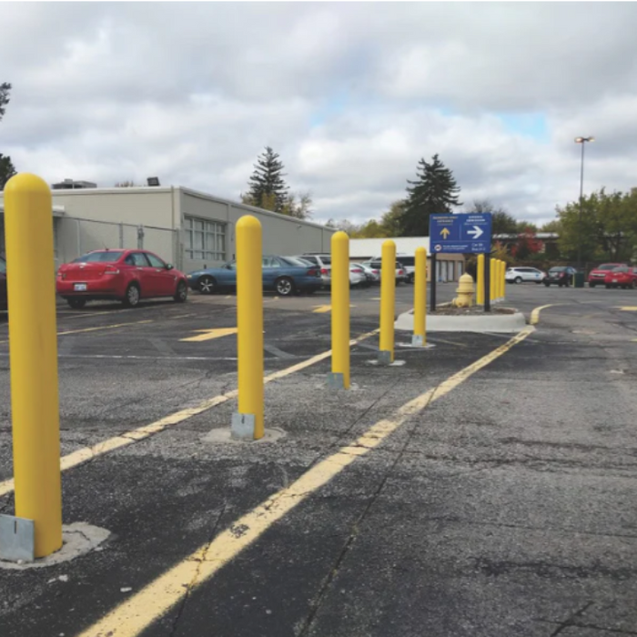 Yellow base plate bollards installed in a commercial parking lot, guiding traffic flow along a designated lane with painted yellow lines.