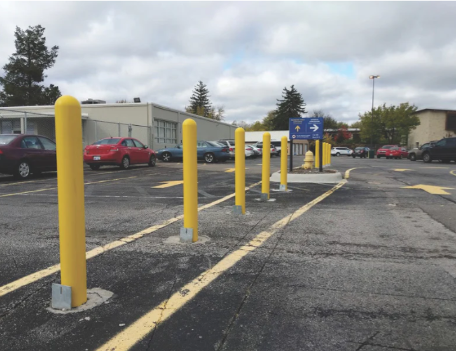 Yellow base plate bollards installed in a commercial parking lot, guiding traffic flow along a designated lane with painted yellow lines.