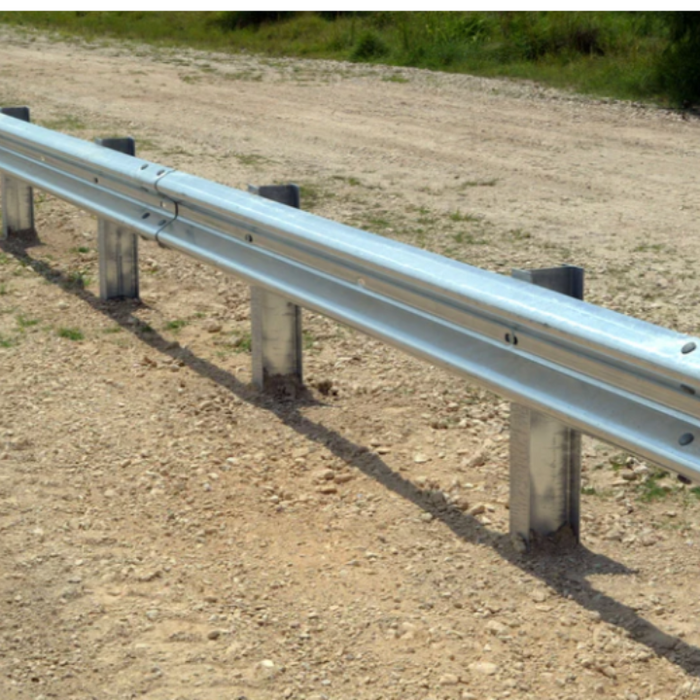 Galvanized steel W-Beam highway guardrail installed on driven posts along a roadside dirt shoulder, showing the corrugated rail profile and splice connections.