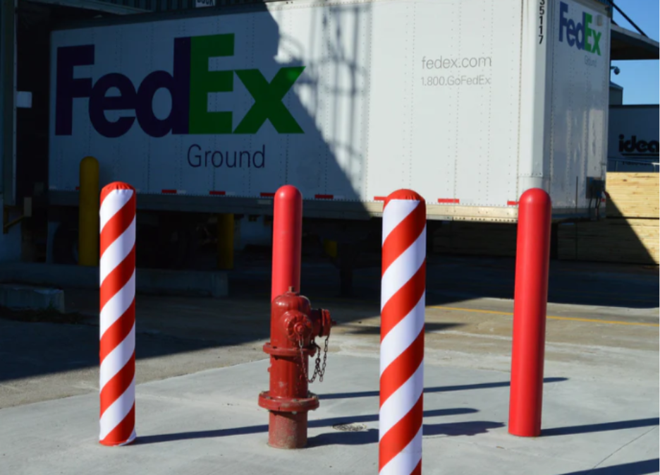  Red and white spiral-striped bollard covers installed at a FedEx Ground loading dock, protecting a fire hydrant and surrounding area from vehicle contact. 