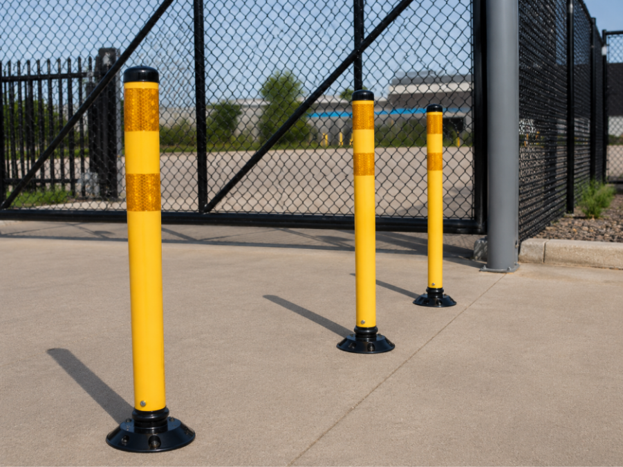 Yellow delineator posts with reflective bands installed on concrete in front of a chain-link security gate. 