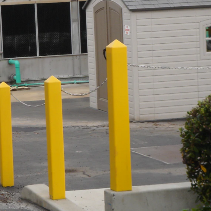 Yellow square bollard covers with pointed tops installed on a commercial property perimeter, connected by a security chain.