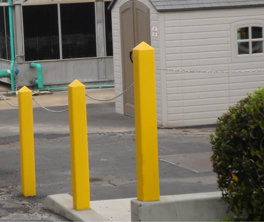 Yellow square bollard covers with pointed tops installed on a commercial property perimeter, connected by a security chain.