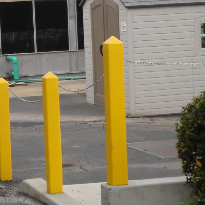 Yellow square bollard covers with pointed tops on a commercial property perimeter, connected by a security chain.