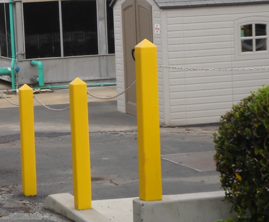 Yellow square bollard covers with pointed tops on a commercial property perimeter, connected by a security chain.