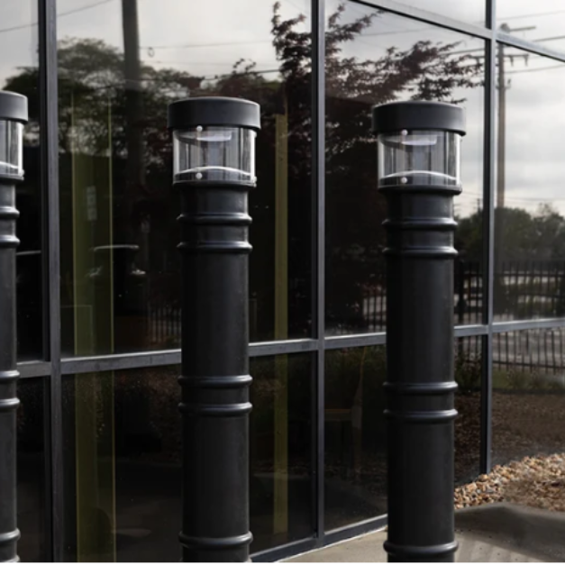  Black lighted bollard covers with integrated light fixtures installed outside a commercial building entrance. 
