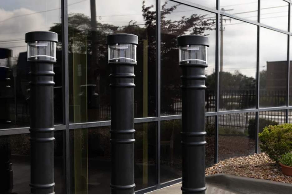  Black lighted bollard covers with integrated light fixtures installed outside a commercial building entrance. 