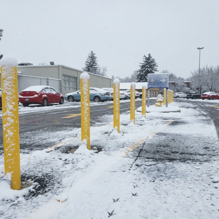 Yellow base plate bollards in a snow-covered commercial parking lot during winter conditions. 