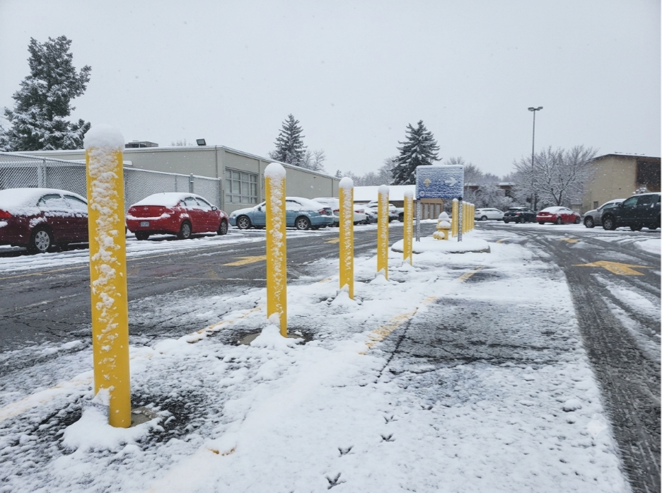 Yellow base plate bollards in a snow-covered commercial parking lot during winter conditions. 