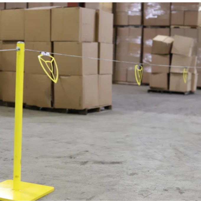 Yellow warning line system stanchions with flagged wire marking a safety boundary in a warehouse. 
