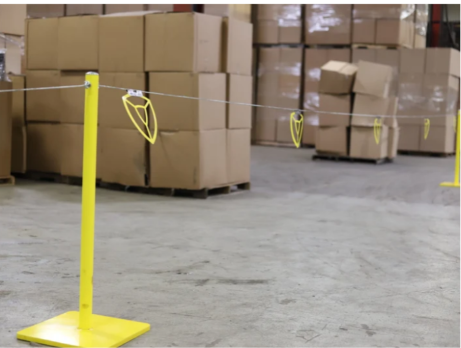 Yellow warning line system stanchions with flagged wire marking a safety boundary in a warehouse. 